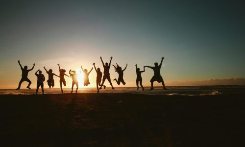 Silhouette of a group of friends jumping on a beach at sunset, expressing joy and freedom.