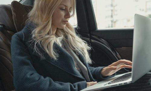 Businesswoman working remotely on a laptop in the backseat of a luxury car. Stylish, modern, and focused.